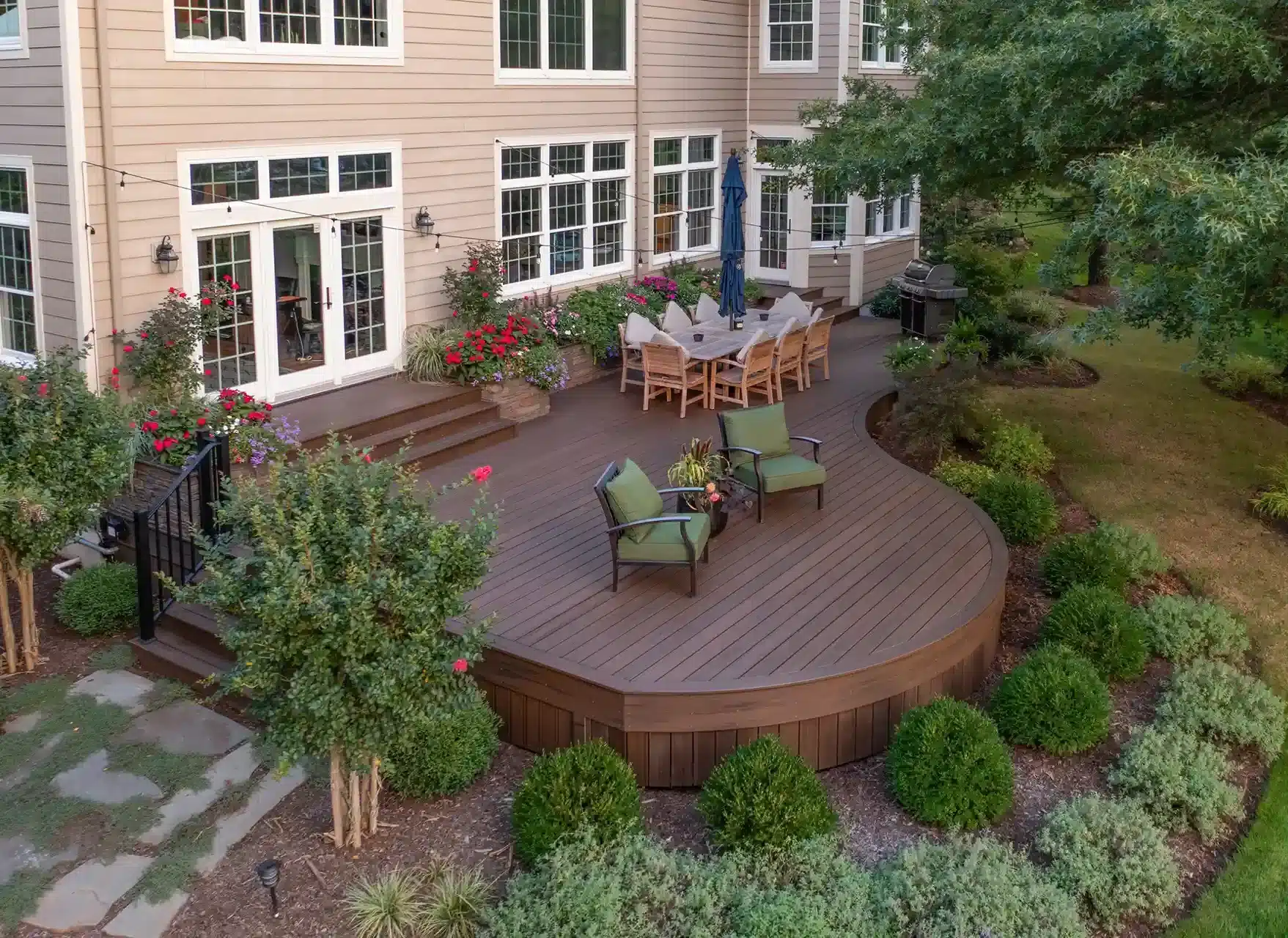 Garden-level deck with curved edges, built-in steps, and a dining area surrounded by vibrant landscaping