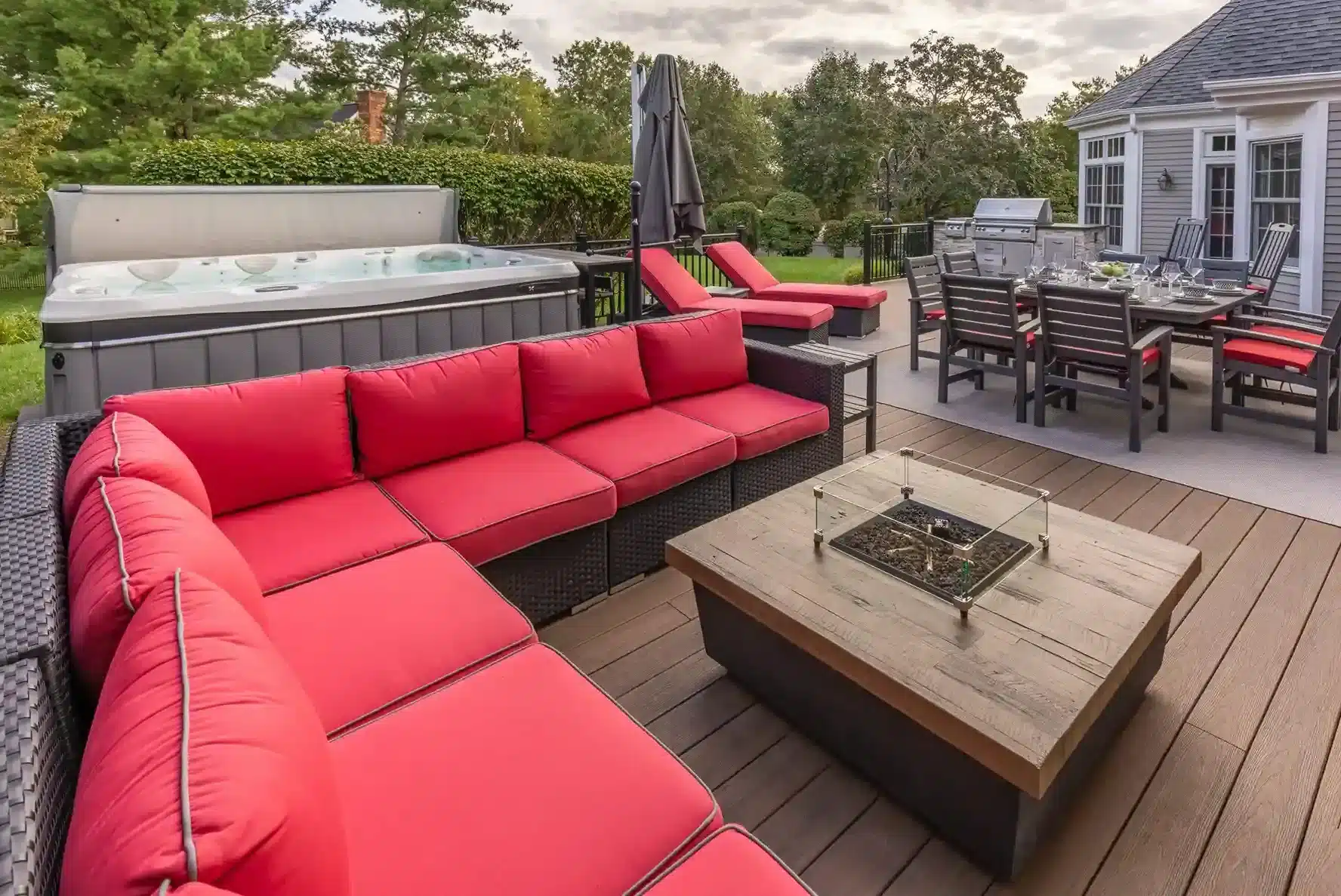 Cozy deck with a red sectional, fire pit, hot tub, and dining space for outdoor entertaining