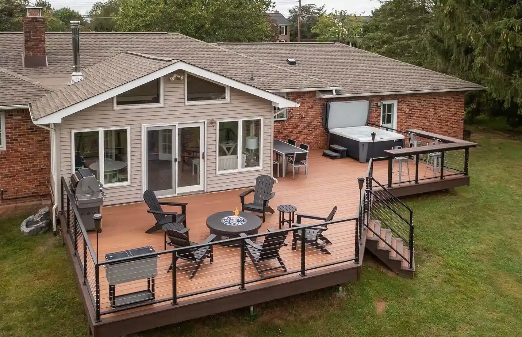 Modern deck with cable railing, a fire pit, hot tub, and bar seating for ultimate relaxation