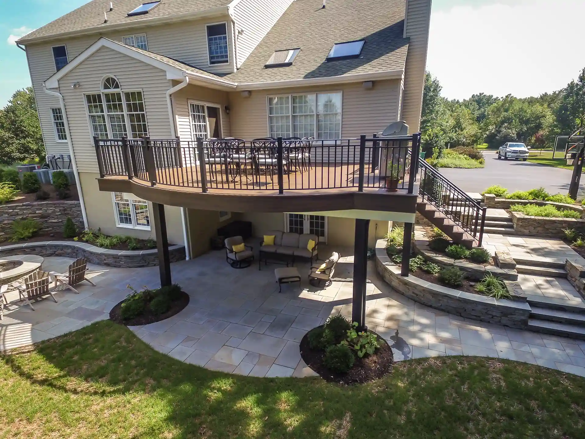 patio builder in central new jersey Photo of a two-story house with a second-floor deck, lower-level patio, fire pit area, and stone retaining walls.