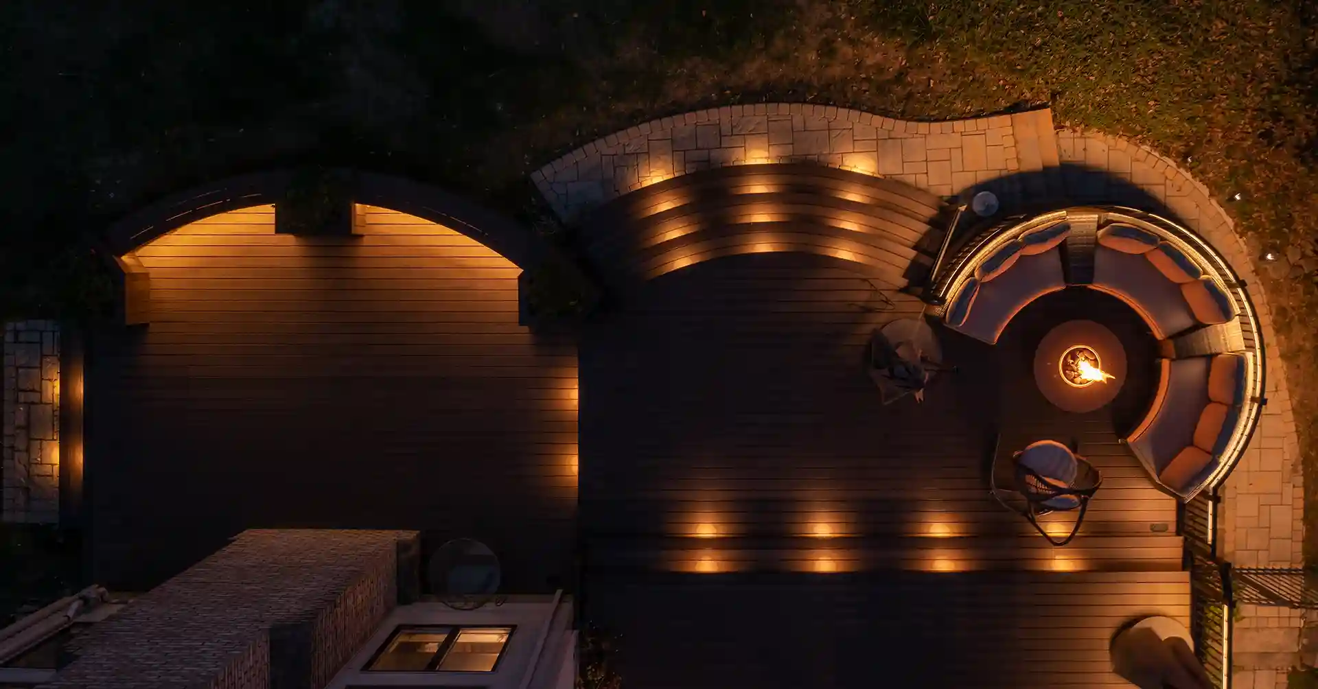 paver patio designs in central new jersey Photo of an elevated deck at night with curved steps, accent lighting, and circular outdoor seating around a fire pit.