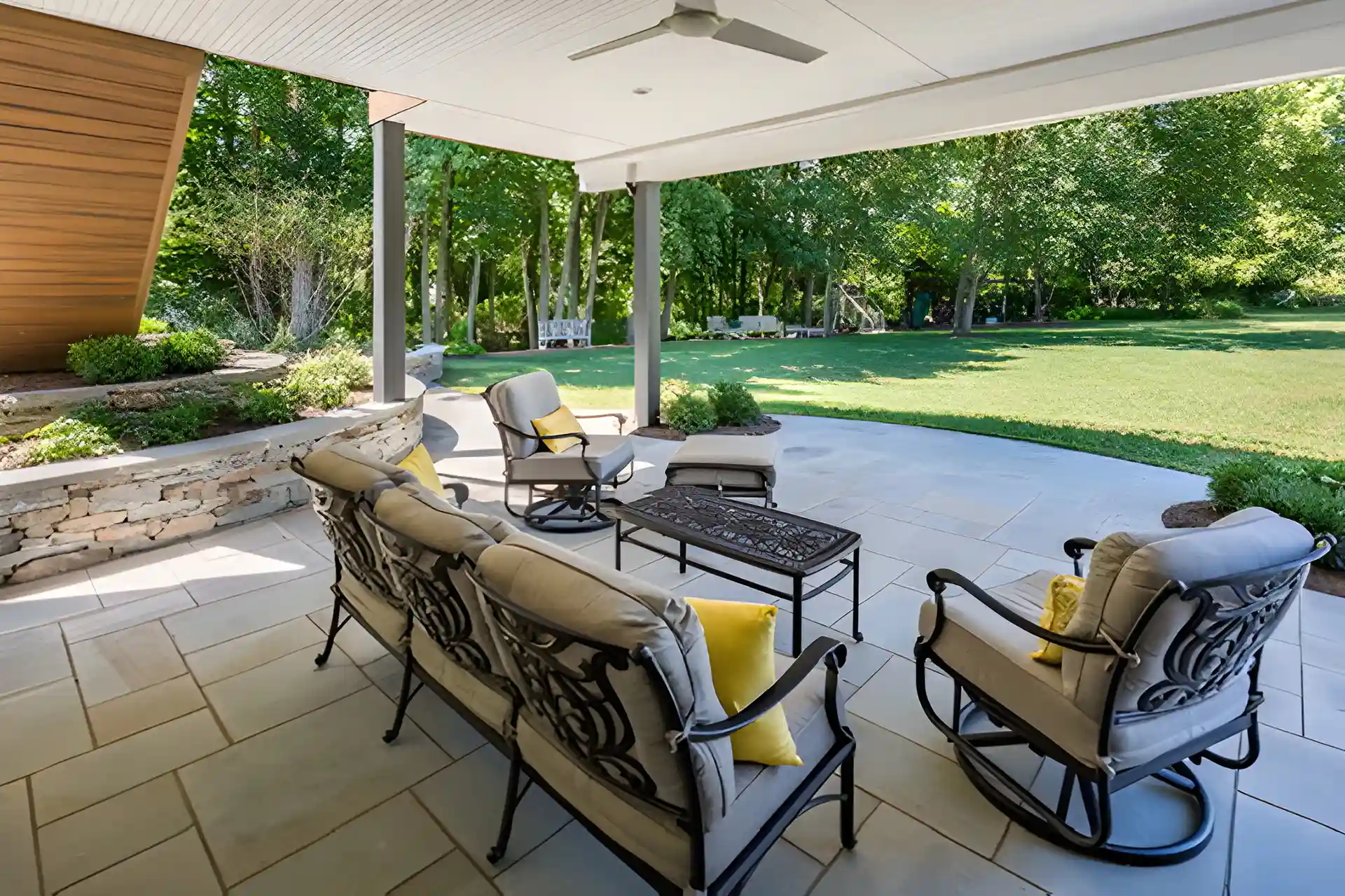 paver patio installation in central new jersey Photo of an outdoor patio with gray stone flooring, covered by a white roof, furnished with a gray and black metal sofa and chairs, overlooking a grassy backyard.