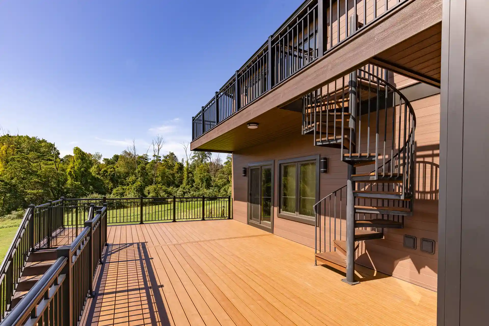 Photo of a spacious deck featuring Trex decking, a spiral staircase, modern railing, and scenic backyard view.