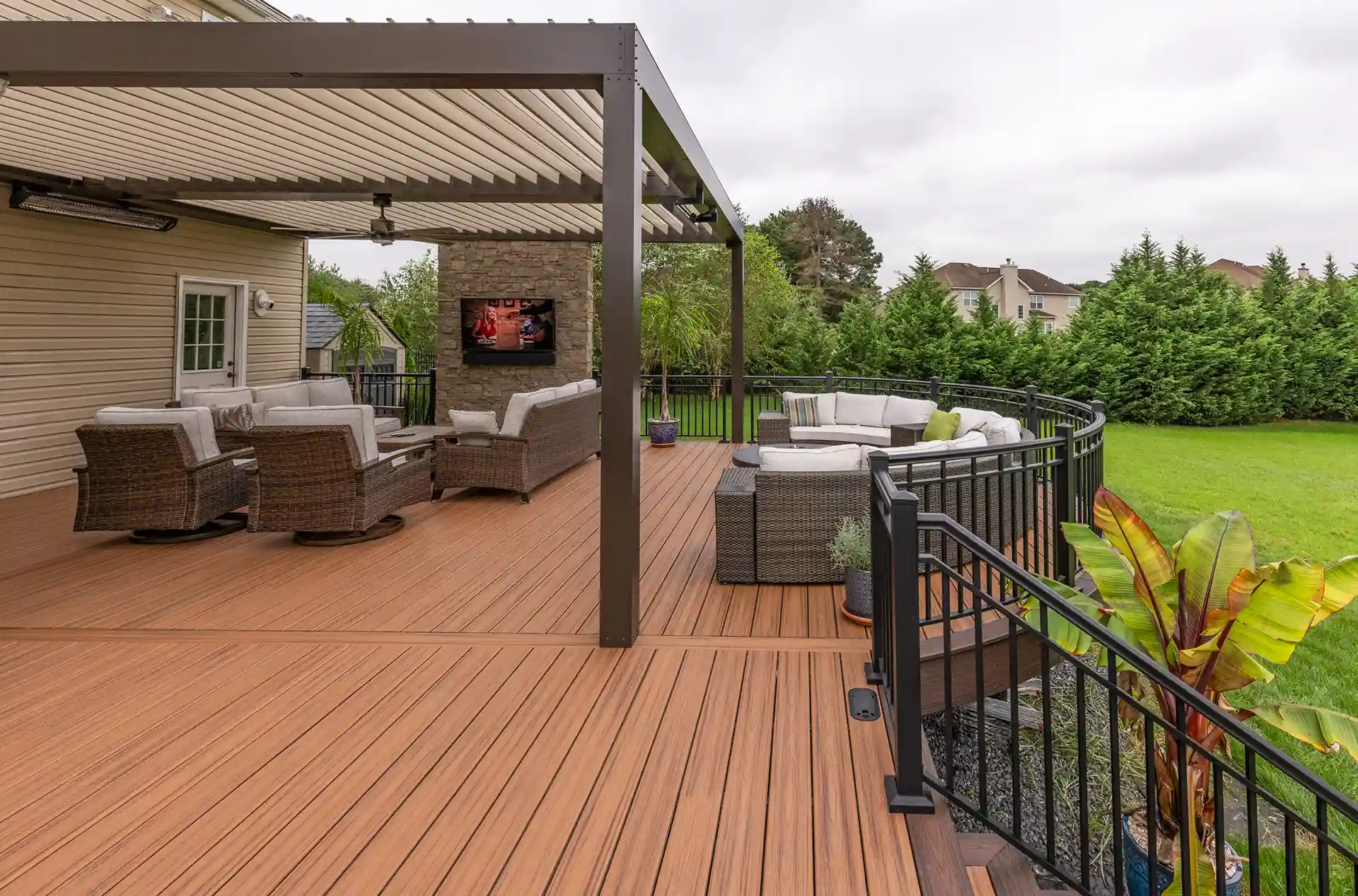Photo of a covered Trex deck with a sectional seating area, TV, and modern black railing.
