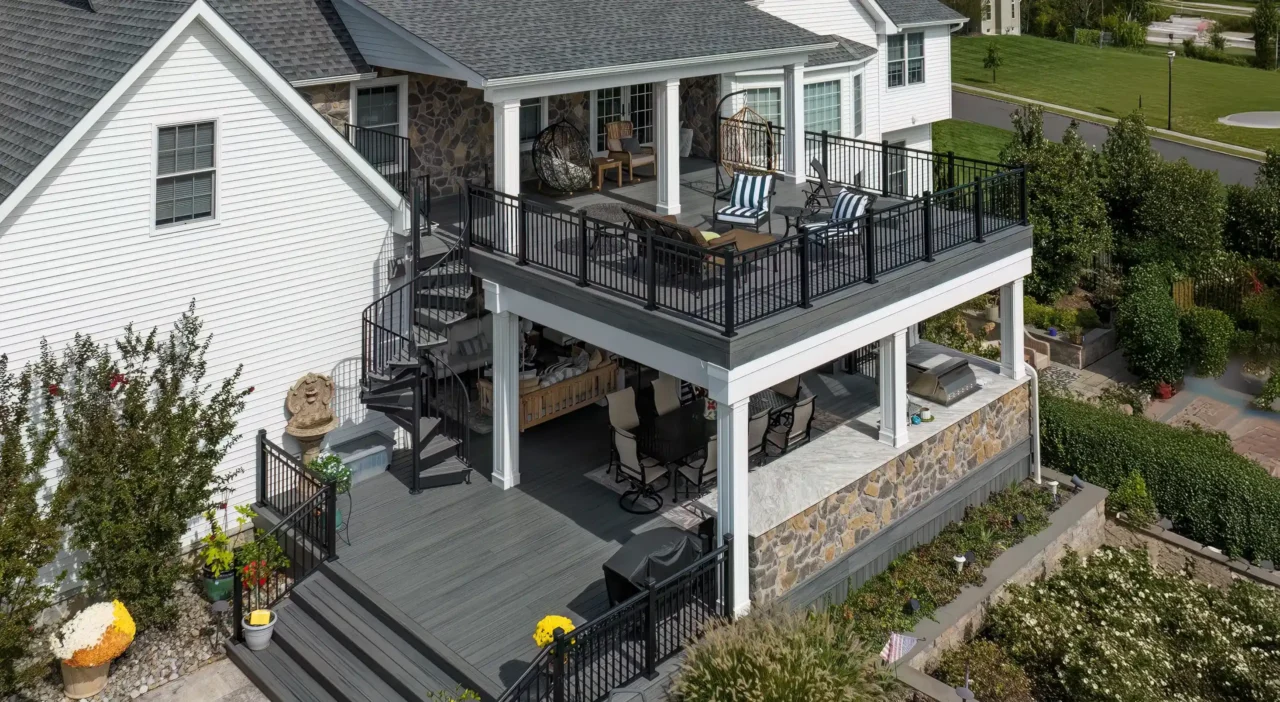 Photo of a covered outdoor dining area with a stone outdoor kitchen, a large table, and metal chairs on a Trex Transcend Island Mist deck with phantom drop screens.
