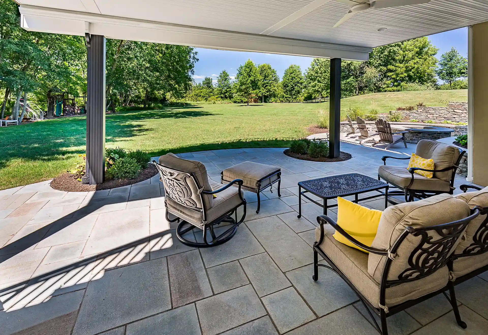 Under-deck patio with stone flooring, cushioned metal chairs, and open view of grassy yard.