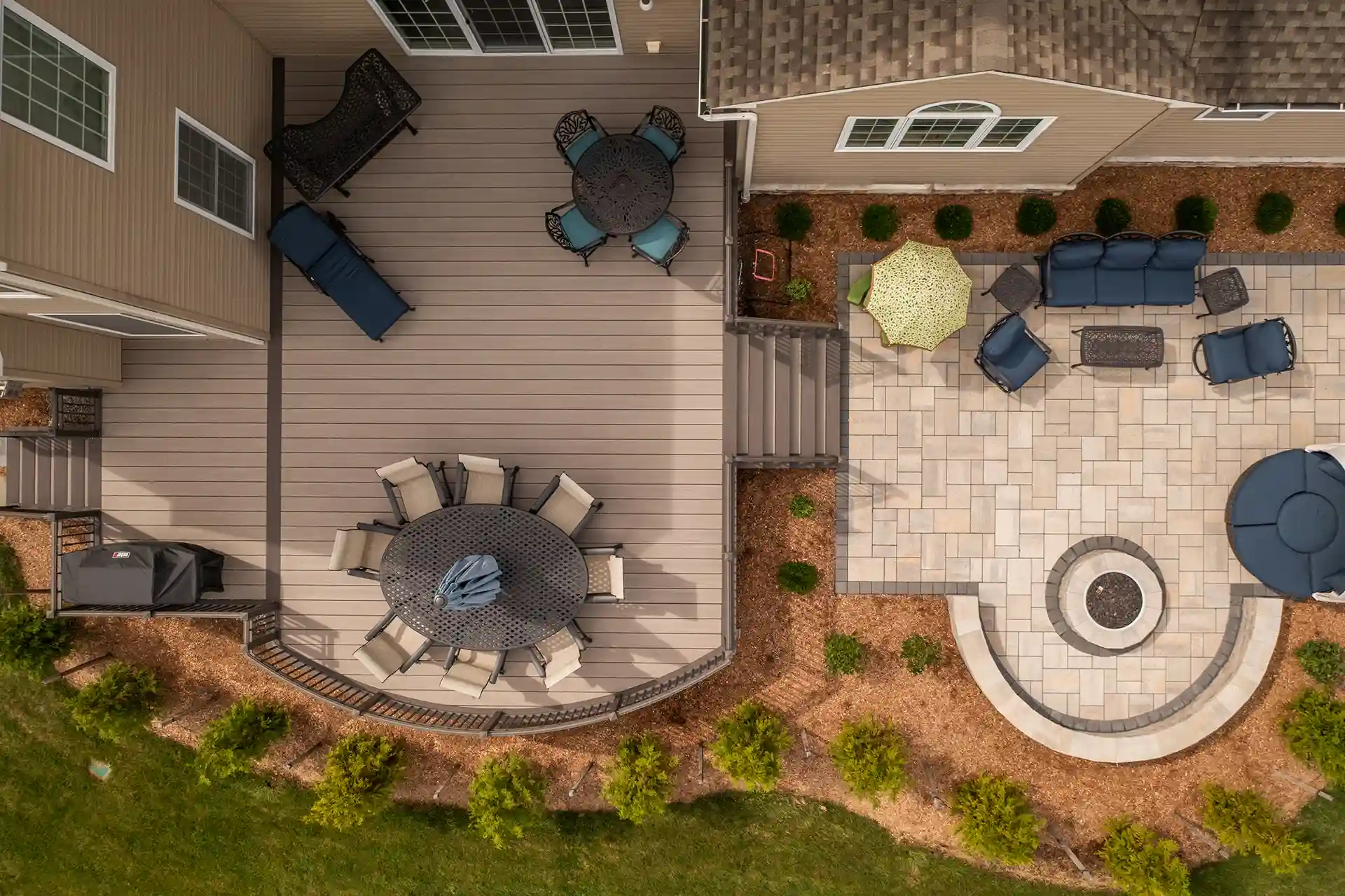 Overhead view of composite deck and stone patio with circular fire pit and lounge furniture.
