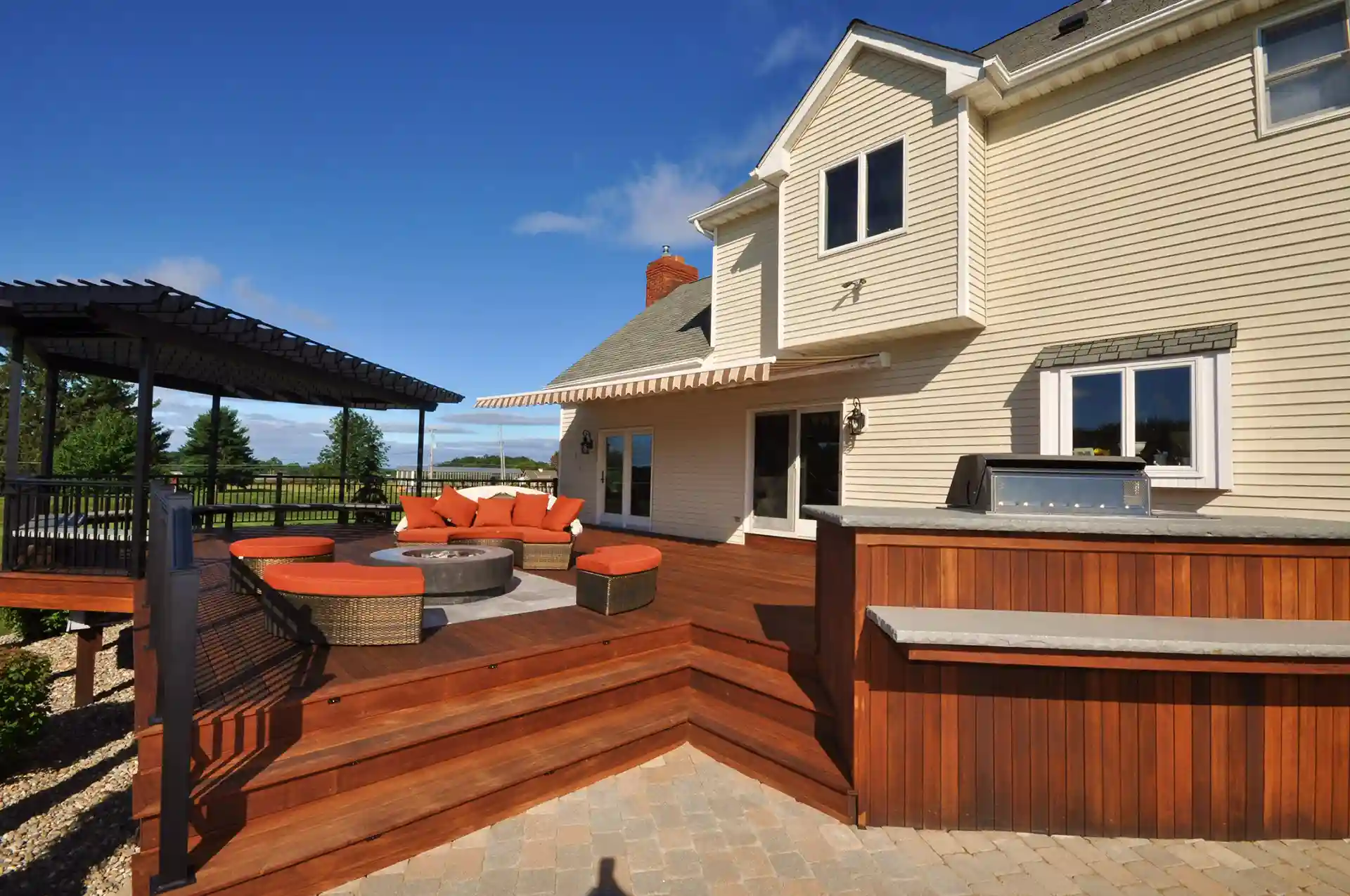 Photo of a wood deck with modern pergola, outdoor furniture, fire pit, and wide deck steps 