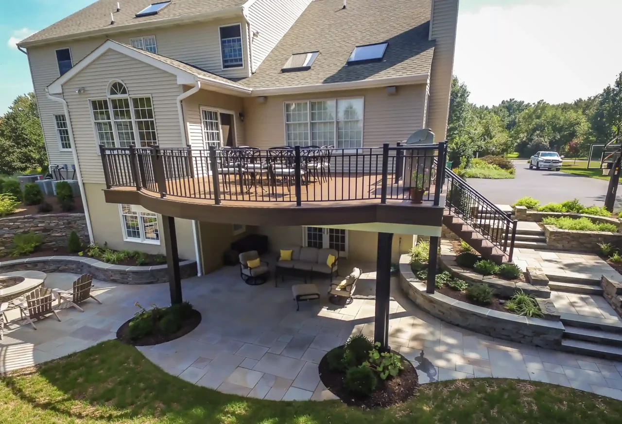 Aerial photo of an elevated deck with deck railing, deck steps, patio, fire pit, hardscaping, and decorative retaining walls.